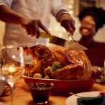 Close-up of black man carving roasted turkey during Thanksgiving meal at dining table.