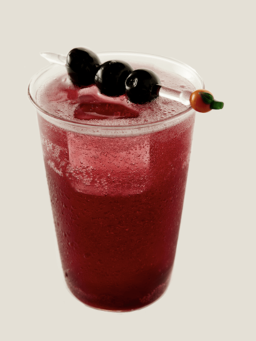 A Lambrusco spritz cocktail in a glass with ice with maraschino cherries on top