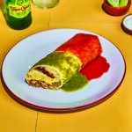 Photo of a New Mexico style breakfast burrito covered in red and green salsa on a white plate.