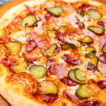 Fresh pizza pickles, bacon, sausages and cheese on a wooden board. Close-up, selective focus