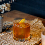 The Campfire Old Fashioned cocktail with an orange peel garnish sitting on a fall tablescape